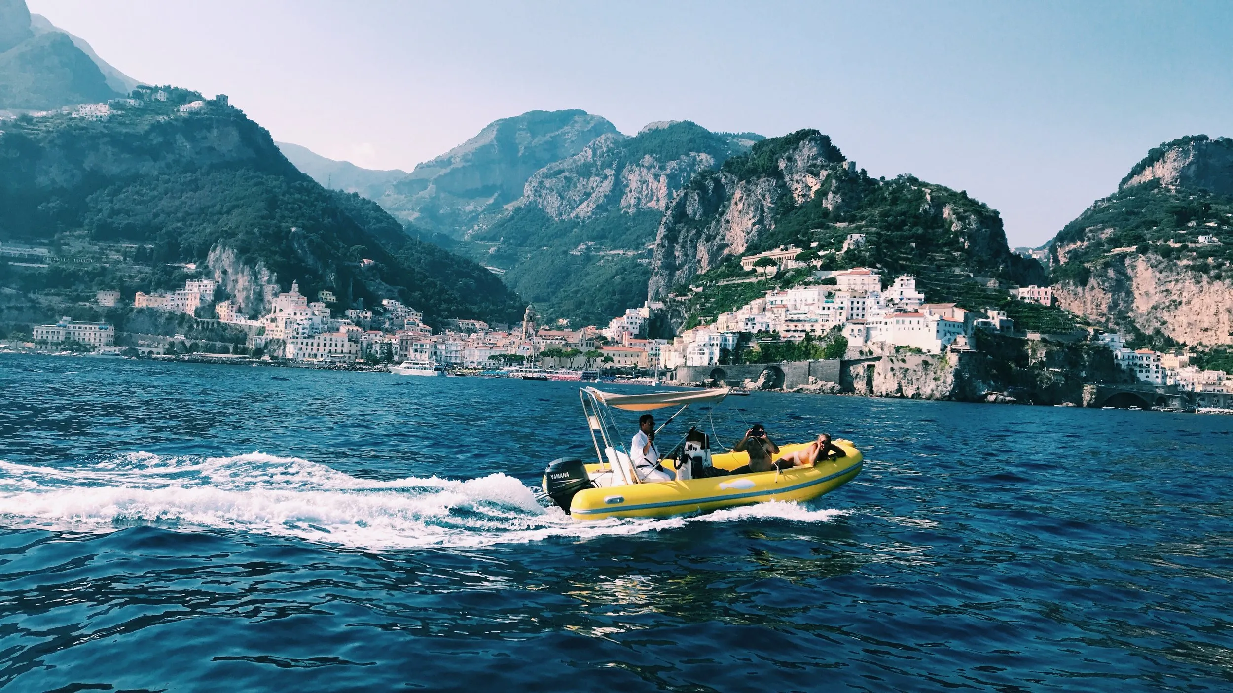 Three people in a yellow inflatable, the town and mountains behind.