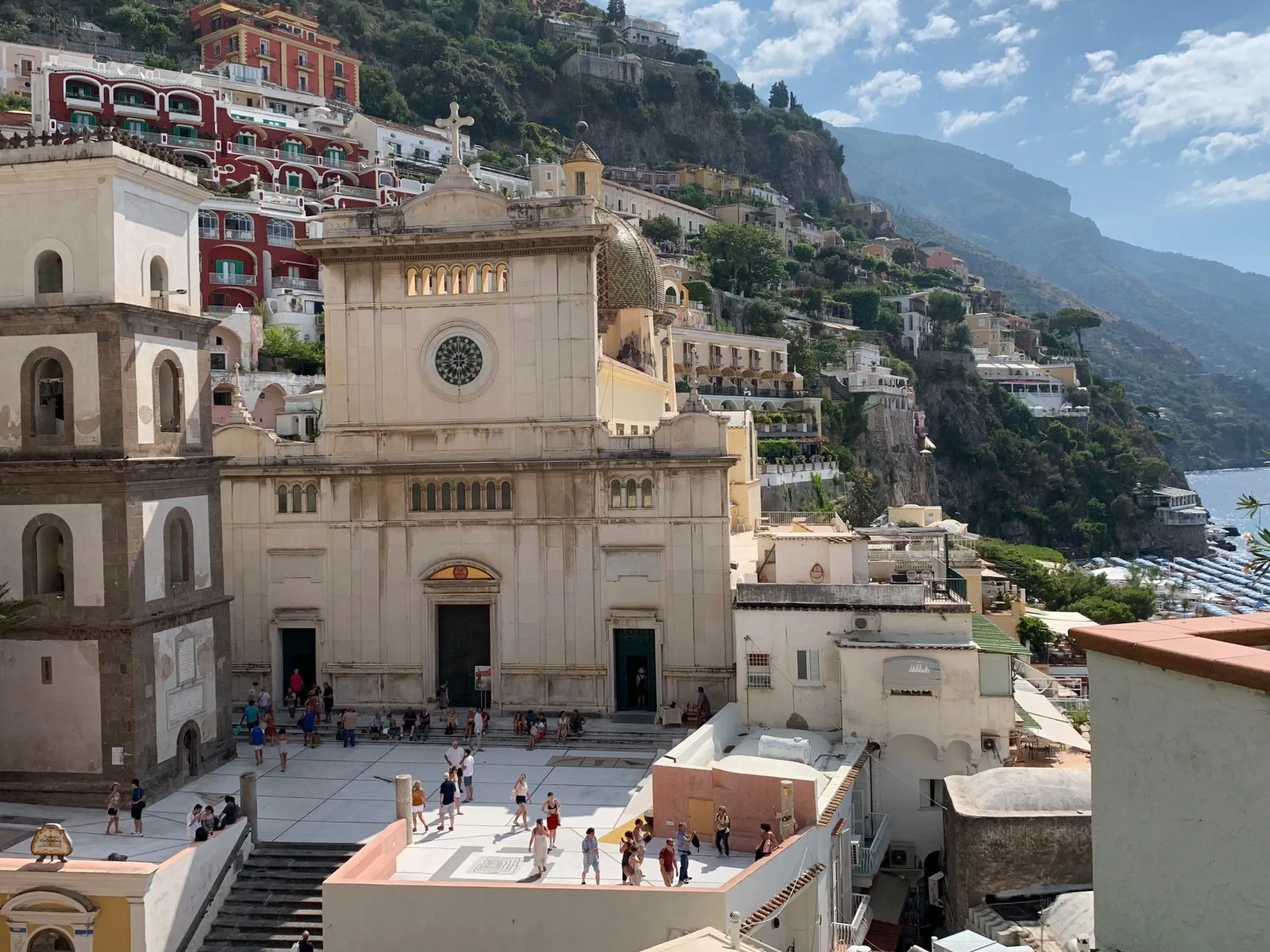 A church with a rose window at the foot of a hill of painted houses.