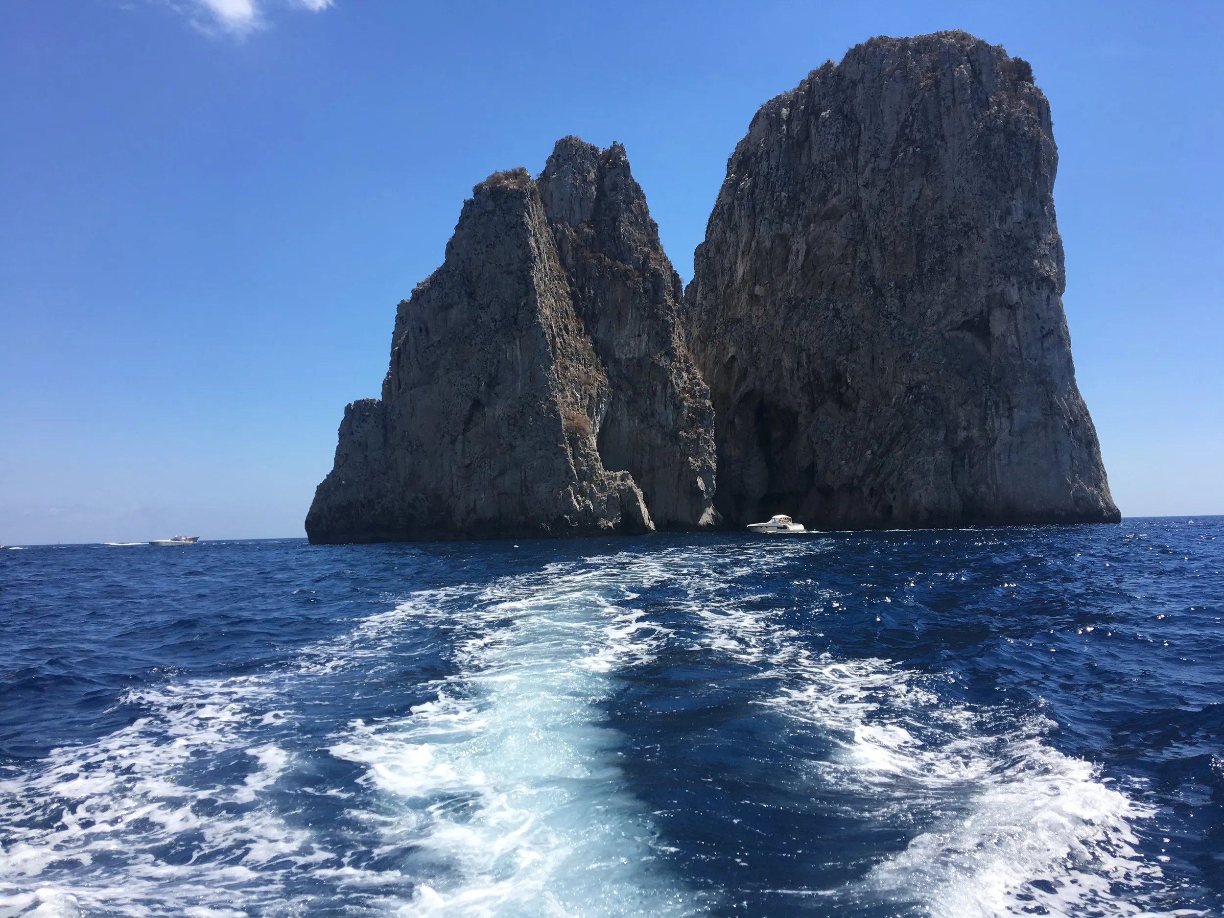 Sea stacks and two boats on a flat blue sea.